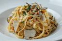 A plate of tagliatelle pasta garnished with thin slices of black truffle, fresh parsley, and a creamy sauce, served on a white dish.