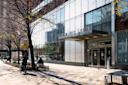 Street view of the Schomburg Center for Research in Black Culture, featuring a glass façade with the name displayed at the entrance. Pedestrians and leafless trees line the sidewalk under a clear sky.