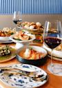 A table set with assorted seafood dishes, including shrimp and mussels, alongside glasses of red wine on a wooden surface with blue and white patterned plates and silverware.