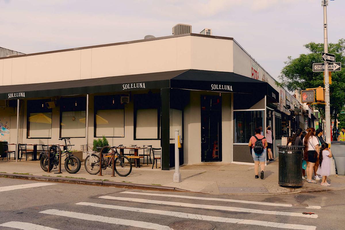 A street corner with the restaurant Soleluna, featuring outdoor seating, bicycles parked nearby, and a group of people standing on the sidewalk near a one-way street sign.
