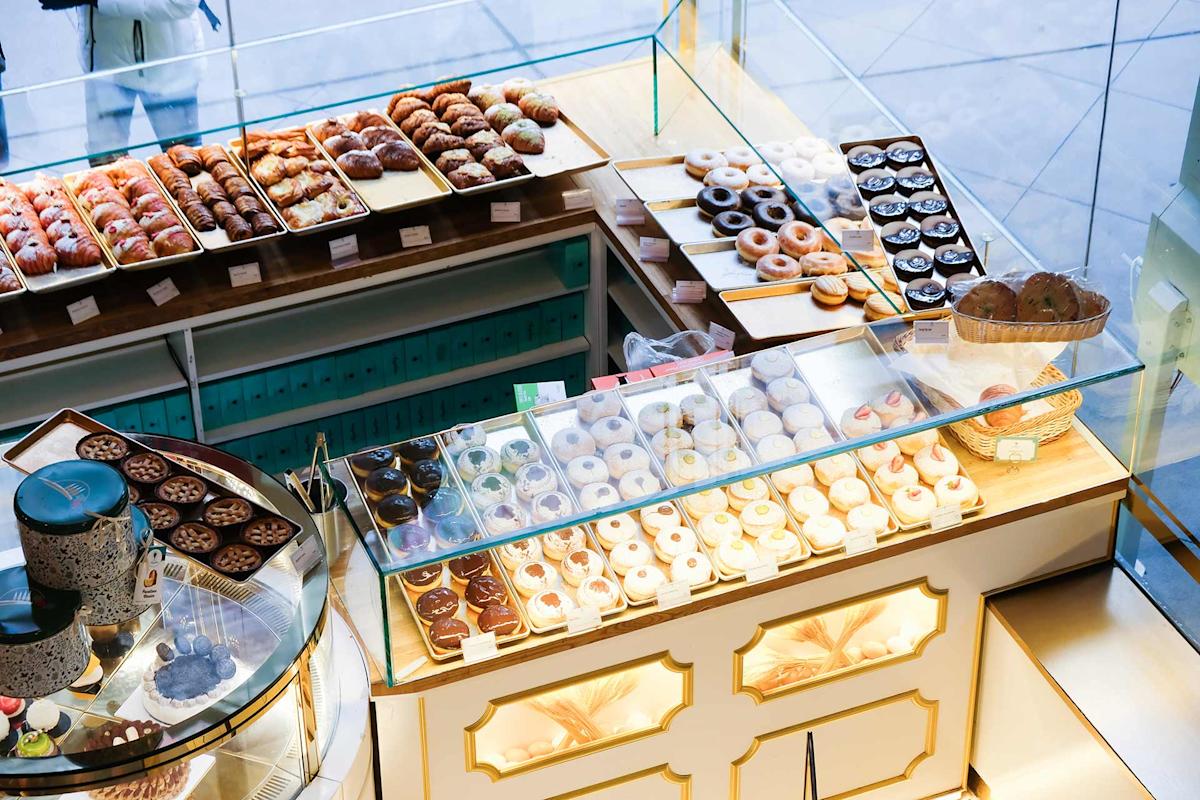 A bakery display filled with assorted pastries, donuts, and baked goods arranged neatly on trays behind glass, with cakes and desserts visible on the counter.