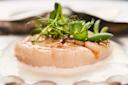 A close-up of a seared scallop topped with fresh green herbs and pea shoots, served on a white creamy sauce with an elegant presentation.