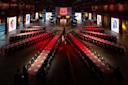 A large event space with a unique seating arrangement in a star pattern. Each row is adorned with red and white tablecloths and table settings. Illuminated screens surround the area, and a central stage displays vibrant graphics.