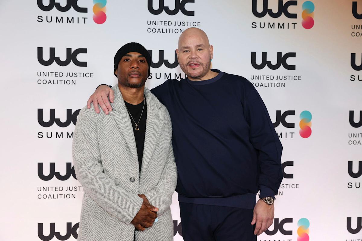 Two men pose together in front of a step-and-repeat backdrop with "United Justice Coalition Summit" logos. One man wears a gray coat and black beanie; the other wears a navy blue outfit with his arm around the first man's shoulder.