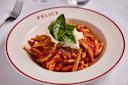 A plate of pasta topped with tomato sauce, burrata cheese, breadcrumbs, and fresh basil leaves, served in a white bowl with a red rim and the word "FELICE" printed on it.