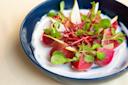 A blue bowl filled with vibrant red beet slices, creamy white yogurt, thin apple slivers, fresh sprigs of greens, and delicate shredded beets on top, creating a colorful and appetizing dish.