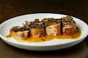 Four slices of roasted chicken roulade topped with sliced mushrooms and herbs, served with a rich, golden-brown sauce on a white plate, set on a wooden table.
