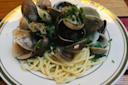 A plate of spaghetti topped with clams in their shells, garnished with chopped fresh herbs, served on a white plate with a green border.