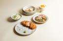A minimalist meal setting with a breaded cutlet, a small mound of wasabi, dipping salt, a bowl of cabbage, grilled fish on rice, a small dish of thinly sliced pork with sauce, and a bowl of fruit dessert.