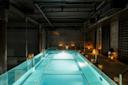 A modern indoor pool with glass sides, illuminated by soft lighting and lanterns placed along the brick walls, creating a serene and luxurious atmosphere.