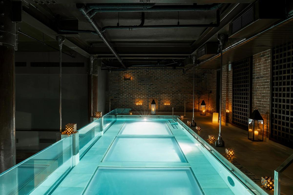 A modern indoor pool with glass sides, illuminated by soft lighting and lanterns placed along the brick walls, creating a serene and luxurious atmosphere.
