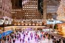 A bustling ice skating rink at night, surrounded by illuminated skyscrapers and decorated with a large, sparkling Christmas tree on the right. Skaters of all ages are enjoying the lively atmosphere.