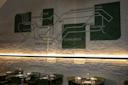 A painted subway map with Korean station names decorates a brick wall above a row of tables and green chairs in a modern, dimly lit restaurant.