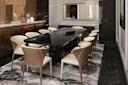 Modern dining room with a black rectangular table, eight cream-colored chairs, a patterned rug, large wall mirror, and light wood cabinetry with decorative items. The room has dark floors and elegant decor.
