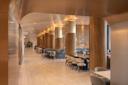 A modern hotel lobby with wooden columns and recessed lighting. The space features comfortable seating with blue and beige tones, tables, and lush greenery. The polished floor adds to the sleek, contemporary design.
