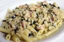 A plate of penne pasta topped with a creamy sauce containing diced zucchini, onions, and bits of bacon or ham. The sauce appears rich and thick, coating the pasta evenly.