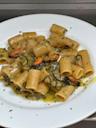 A white plate of rigatoni pasta mixed with mussels and zucchini in a light herb sauce, garnished with chopped parsley.