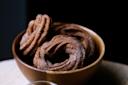 A wooden bowl filled with three round, ridged, sugar-coated churros sits on a light surface, with a dark background behind them.