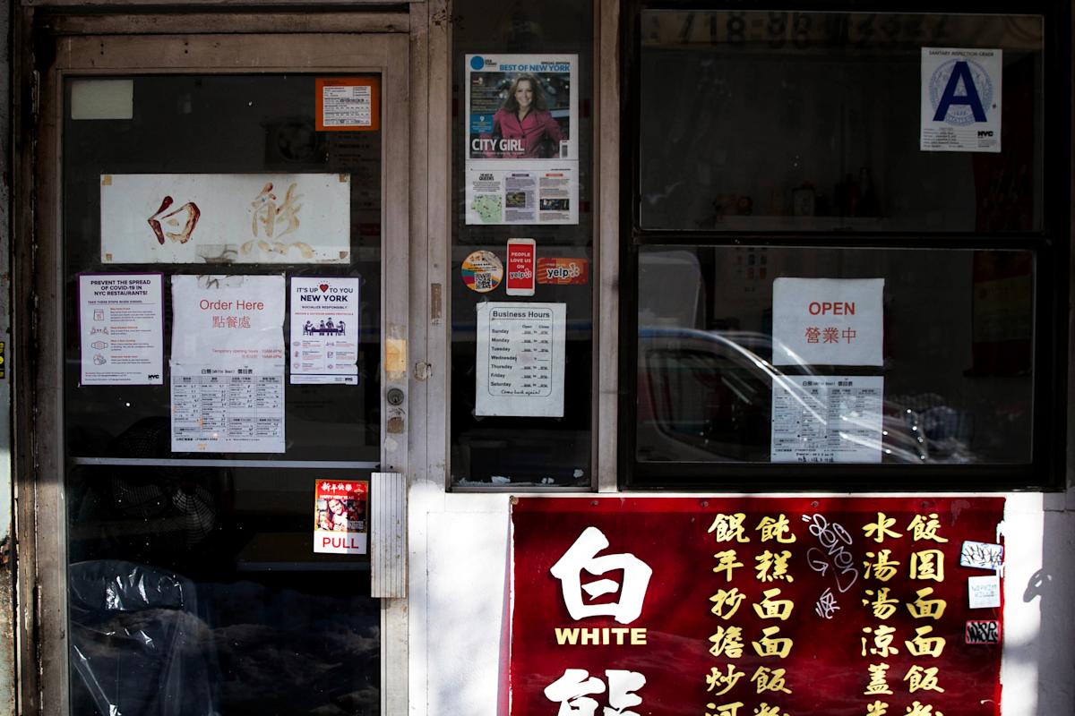 A storefront window with Chinese and English signs, including menus, business hours, and an "OPEN" sign. There is a restaurant grade "A" sticker and various posters and notices on the door and window.
