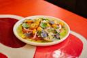 A colorful tomato salad with yellow and red tomatoes, red onion slices, fresh basil leaves, and seasoning, served on a white plate atop a red and tan table.
