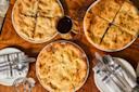 Four round khachapuri breads on plates, two cut into slices, with a glass of red wine, empty plates, utensils, and a glass of water on a wooden table.
