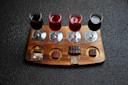 A wooden board displays four glasses of red wine paired with different pieces of chocolate. Each glass has a unique type of chocolate beside it, ranging from bars to square pieces, arranged neatly on the textured surface.