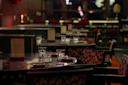 A dimly lit restaurant with empty tables set for dining. Tables are adorned with water glasses, cutlery, and menus. The seating features patterned upholstery, and soft lighting creates a cozy ambiance.