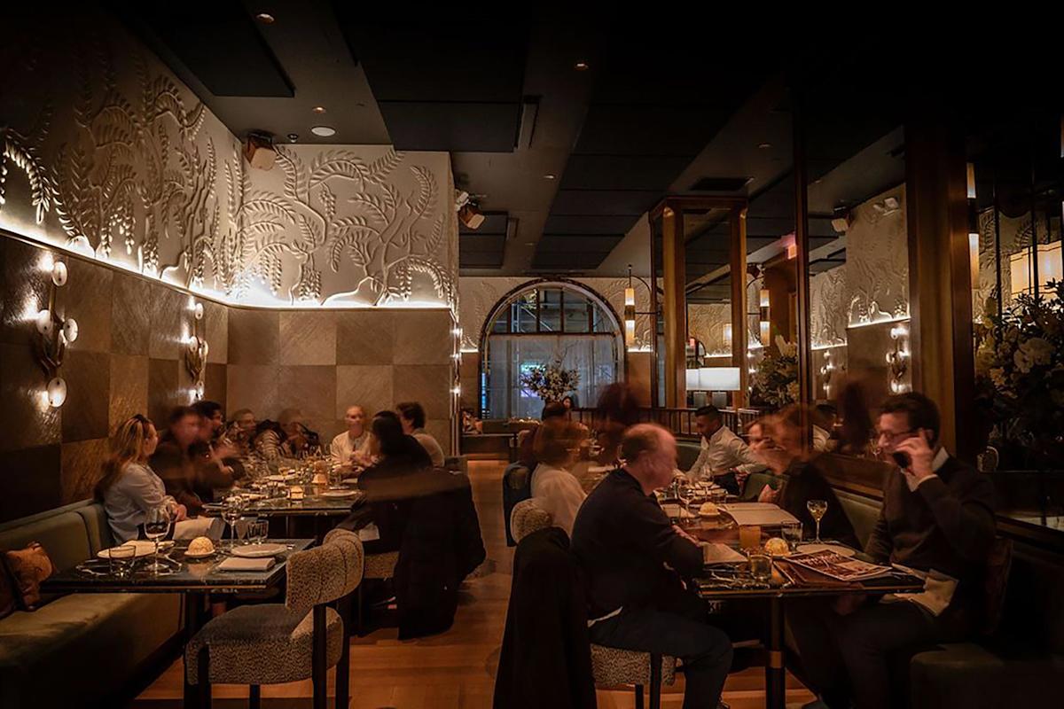 A warmly lit restaurant with elegant wall decor and several groups of people dining and conversing at tables, creating a lively and cozy ambiance.