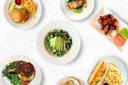 A collage of various dishes on a white background: a burger with fries, salmon with asparagus, a kale salad with avocado, chicken wings with celery and carrots, a steak with greens, and a sandwich with fries.