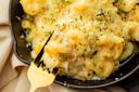 A close-up of creamy baked macaroni and cheese in a skillet, topped with golden breadcrumbs and herbs, with a fork lifting a cheesy bite.