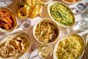 A table set with various Italian pasta dishes, fried vegetables, shrimp in tomato sauce, ravioli, and glasses of water and white wine, all served on patterned plates and bowls.