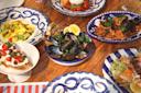 A wooden table set with colorful ceramic dishes holding various Italian foods, including mussels, pasta with seafood, bruschetta, salad, and stuffed pasta, each garnished with fresh herbs and lemon.