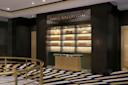 A modern, elegant hallway with a gold and navy patterned carpet, a brass railing, and a sign reading "Paris Ballroom" above a marble and gold reception desk with illuminated shelves behind it.