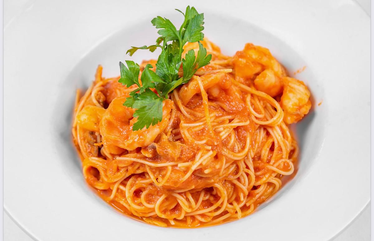 A plate of spaghetti in a rich tomato sauce, garnished with fresh parsley and pieces of shrimp, served in a white bowl.