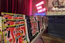 A table displays colorful, abstract art books in front of a neon sign reading "UNDER THE ARCH @ POWERHOUSE" inside a bookstore with stacked books and dark curtains in the background.