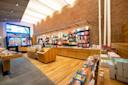 A modern bookstore with wooden shelves and tables displaying colorful books and gifts, large windows letting in natural light, and exposed brick walls creating a cozy atmosphere.