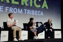 Three people sit on stage at Tribeca Festival, talking into microphones. The person in the center holds up a T-shirt reading "TOTALLY IMPARTIAL POTENTIAL JUROR" while the person on the right laughs. Event signage is visible behind them.