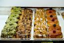 A display case filled with assorted pastries, including ones topped with green and dark chocolate, caramel drizzle, white icing, and round donuts with glossy caramel glaze topped with raspberries and blackberries.