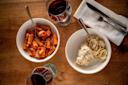 Two bowls of pasta, one with tomato sauce and the other with creamy white sauce, are on a wooden table with two glasses of red wine, a napkin, and silverware.