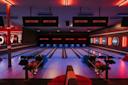A modern bowling alley with multiple lanes, colorful bowling balls, digital screens displaying “Lucky Strike,” and vibrant lighting creating a lively atmosphere.