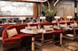 A stylish restaurant interior featuring red upholstered booths, wooden chairs, set tables with glassware, modern lighting, a large wall art piece, and a tall vase with green foliage.