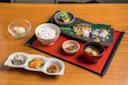 A Japanese meal set on a wooden table. It includes grilled fish, white rice, miso soup, pickles, tofu, and a dessert with green ice cream. The dishes are elegantly arranged on different plates and bowls.