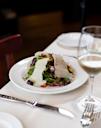 A white plate with mixed greens, olives, tomatoes, and large slices of cheese, set on a white tablecloth beside a wine glass, fork, and knife.
