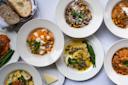 An overhead view of plates with various Italian dishes, including pasta with red and white sauces, ravioli with green beans, gnocchi, bread slices, and a serving of butter, all arranged on a white tablecloth.