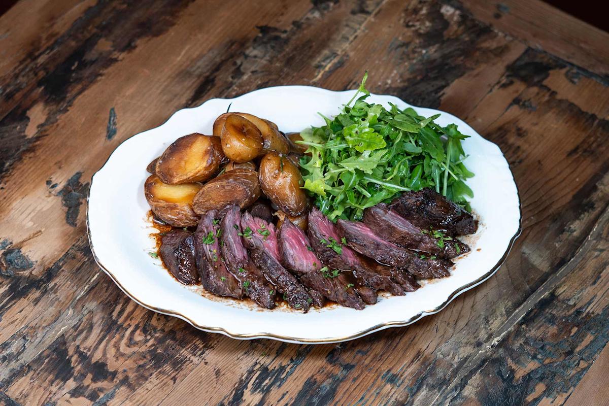 A white plate with sliced steak, roasted potatoes, and a fresh green salad on a rustic wooden table.