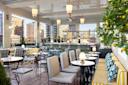 Chic rooftop restaurant with striped bench seating, cushioned chairs, marble tables, hanging lights, and city views through large windows. A lemon tree decorates the corner.