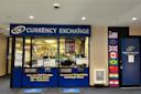 A currency exchange storefront with signs reading "Buy and Sell Foreign Currency from 80+ Countries" and "Extremely Competitive Exchange Rates." Flags of several countries are displayed beside the entrance.