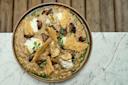 A gourmet dish featuring creamy risotto topped with truffle slices, mushrooms, dollops of creamy cheese, and golden parmesan crisps. It is garnished with fresh herbs and presented on a wooden table.