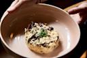 A person holds a beige bowl with creamy mushroom risotto garnished with chopped herbs in the center.