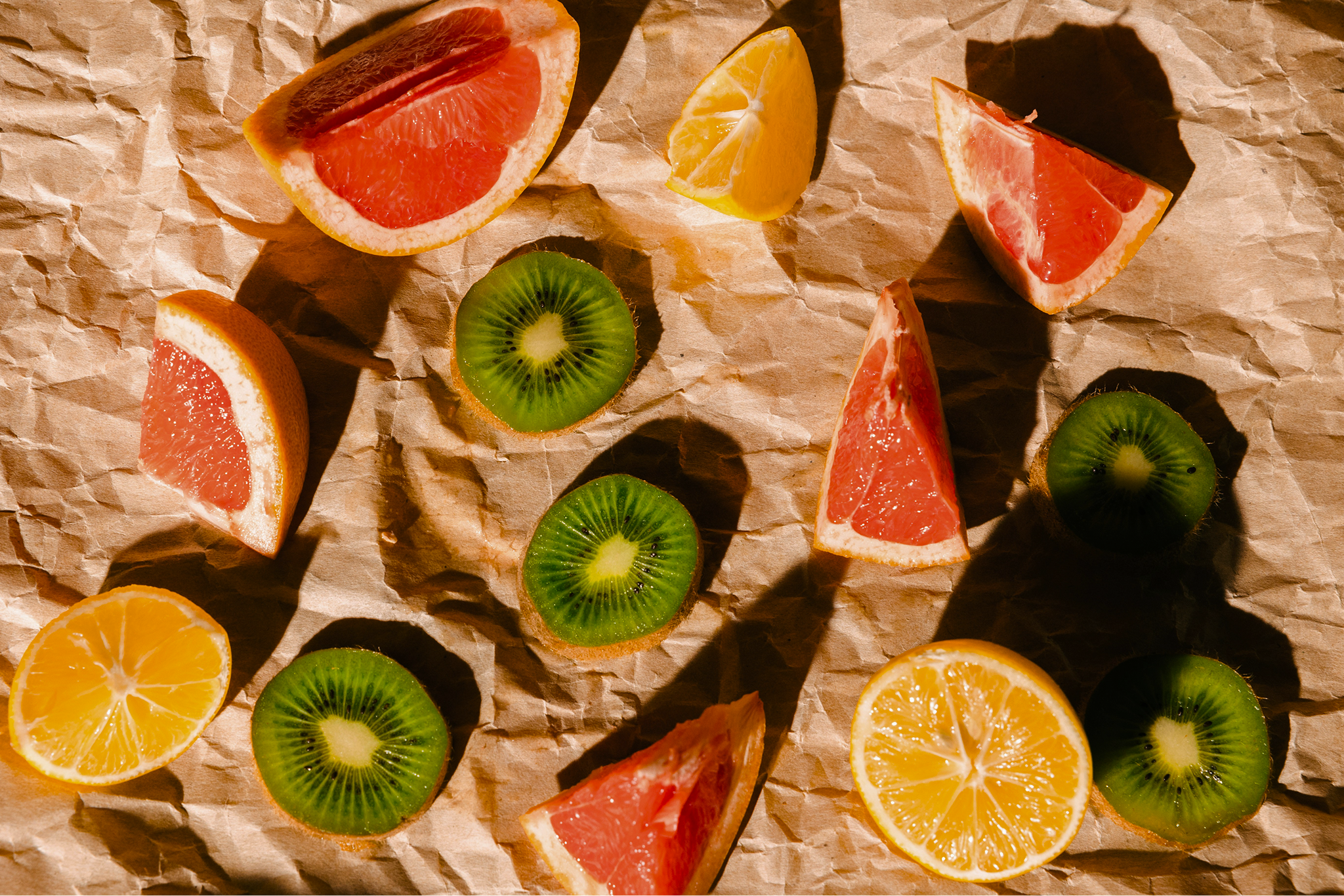 Artful still life of sliced grapefruit, orange, and kiwi on crumpled kraft paper — vibrant, fresh fruit arrangement suggesting healthy, wholesome ingredients
